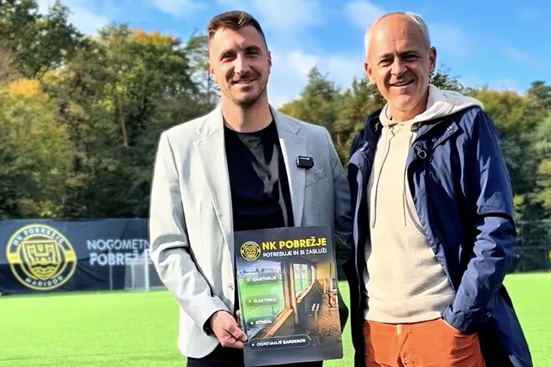 Skupna fotografija ob obisku NK Pobrežje na igrišču z umetno travo in s plakatom o potrebah kluba.