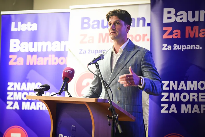 Govorec za pultom z mikrofoni med predstavitvijo programa.