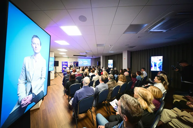 Dvorana z udeleženci in zaslonom med predstavitvijo programa.